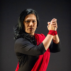 A Filipina woman in a red sash poses against a black background.