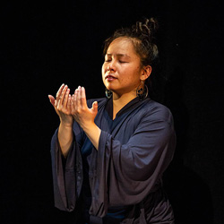 A Southeast Asian woman in a dark blue robe poses against a black background.