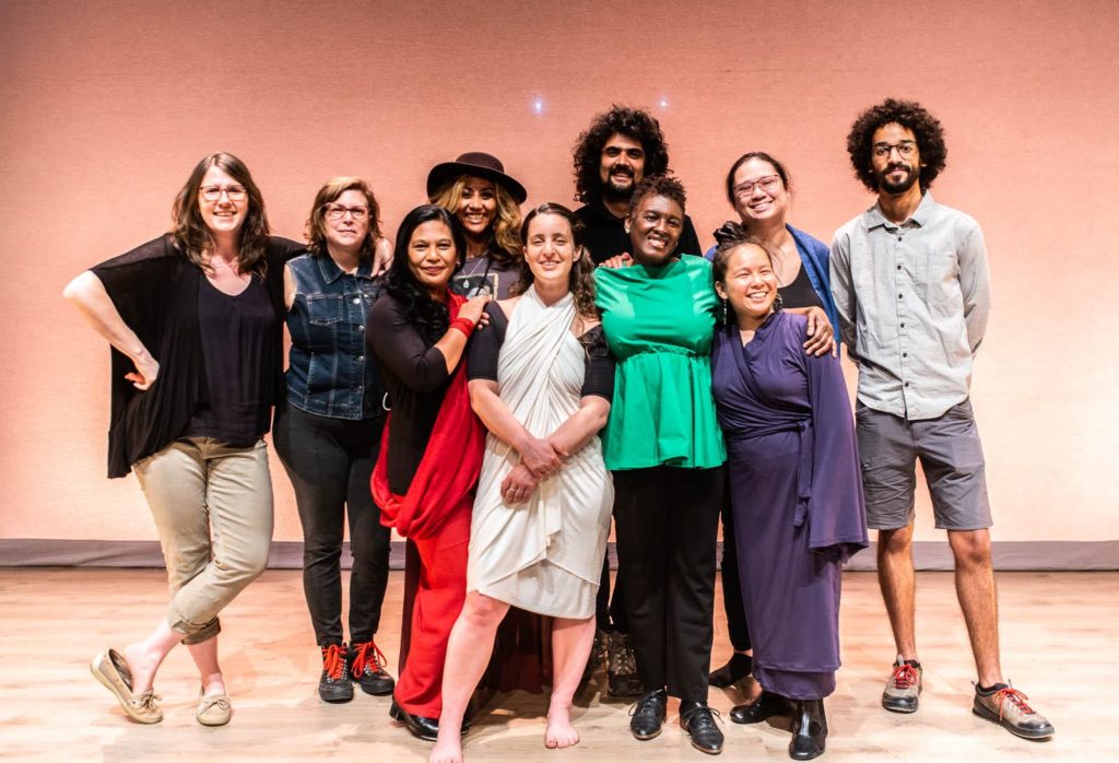 A photo of 10 people standing on stage in front of an orange background, smiling at the camera.