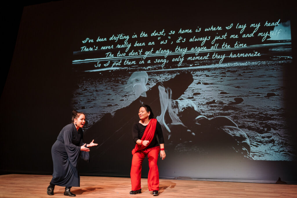 Two Speaking Vibrations artists on stage in performance. One is wearing a blue robe. One is wearing red pants and red sash.