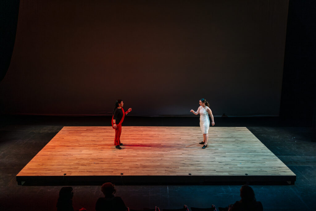 Two Speaking Vibrations performers on stage during the tap dance scene. One is wearing red, the other is wearing white.